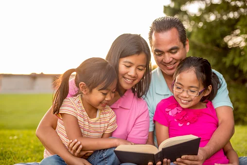 A mother, father and two daughters reading a Bible together outdoors